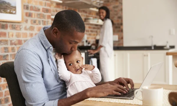 Dad holds toddler while working on laptop