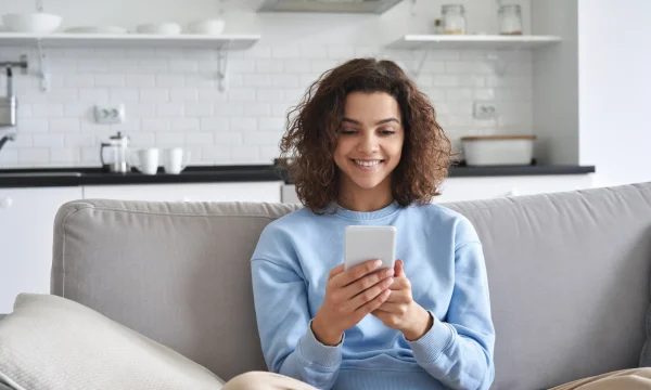 woman on couch smiling while texting