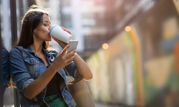 woman drinks coffee while texting on phone